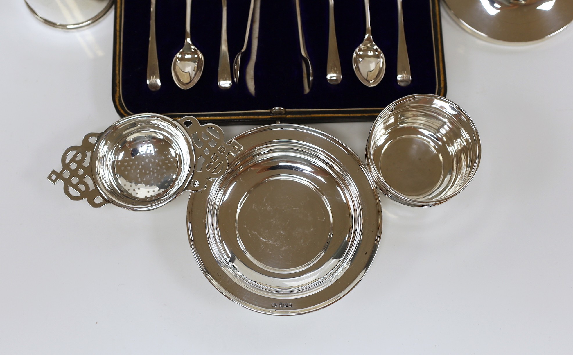 Small silver including a mounted inkwell, tea strainer on stand, mustard pot, small dish and cased set of six coffee spoons with sugar tongs.